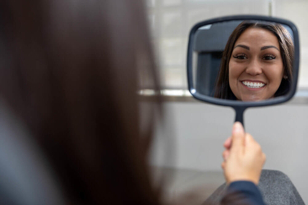 a dental patient looking in a mirror and admiring her new smile